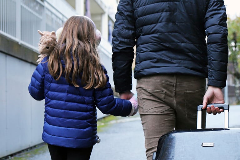 A man and a little girl walking down a street holding hands.