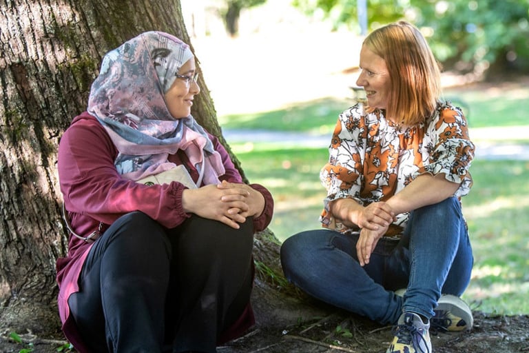 A couple of women sitting next to a tree.